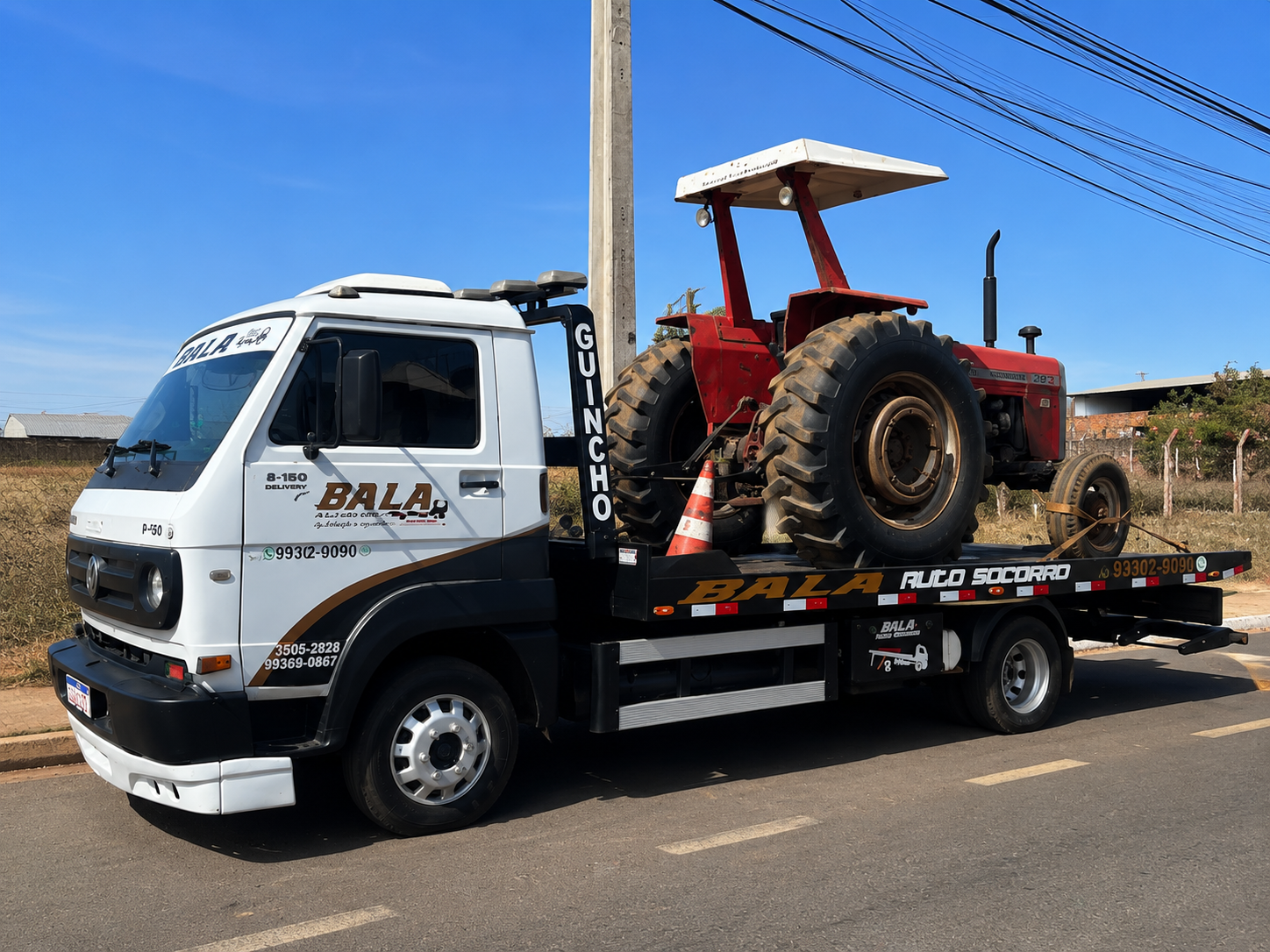 Guincho Bala Auto Socorro transportando um trator vermelho em área urbana